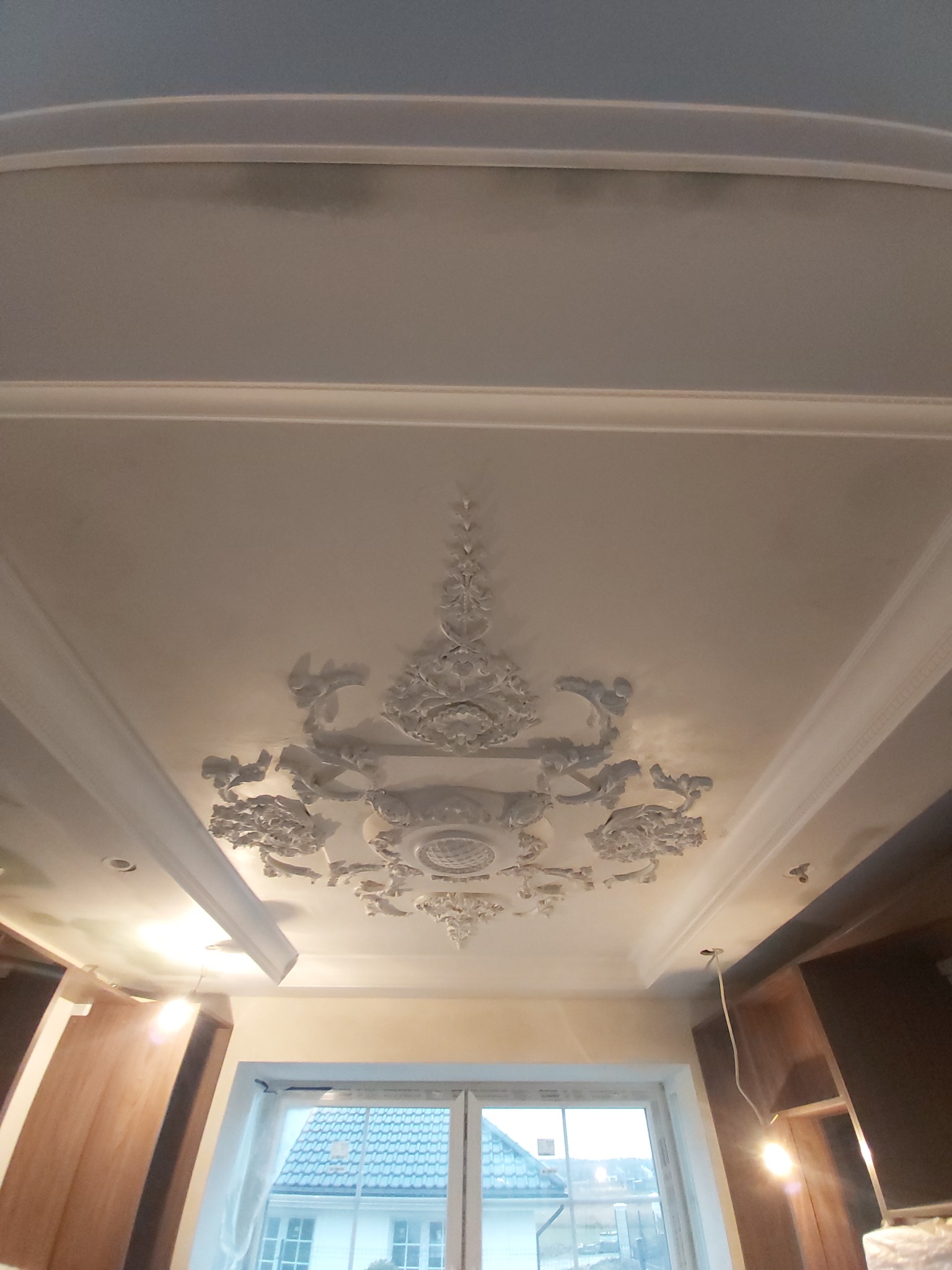 Dekoracyjny sufit z gipsowymi ornamentami w mieszkaniu w Gdyni, widok z dołu na białe listwy i rozety.