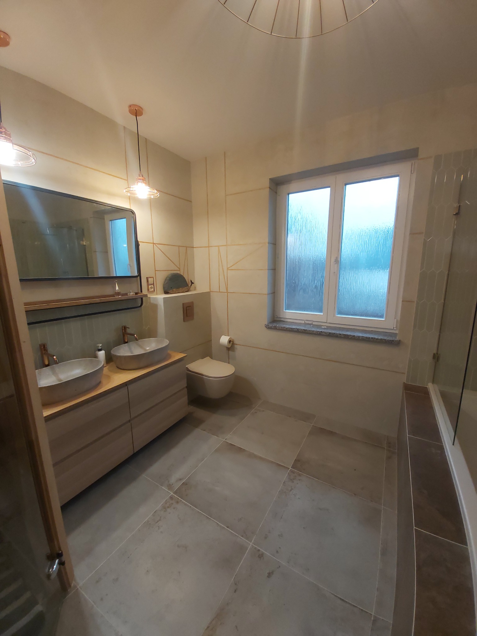 Nowoczesna łazienka z dwoma umywalkami nablatowymi o owalnym kształcie, drewnianą szafką pod umywalkami z szufladami, szarą płytką podłogową, oknem z widokiem na zewnątrz i geometrycznym wzorem...