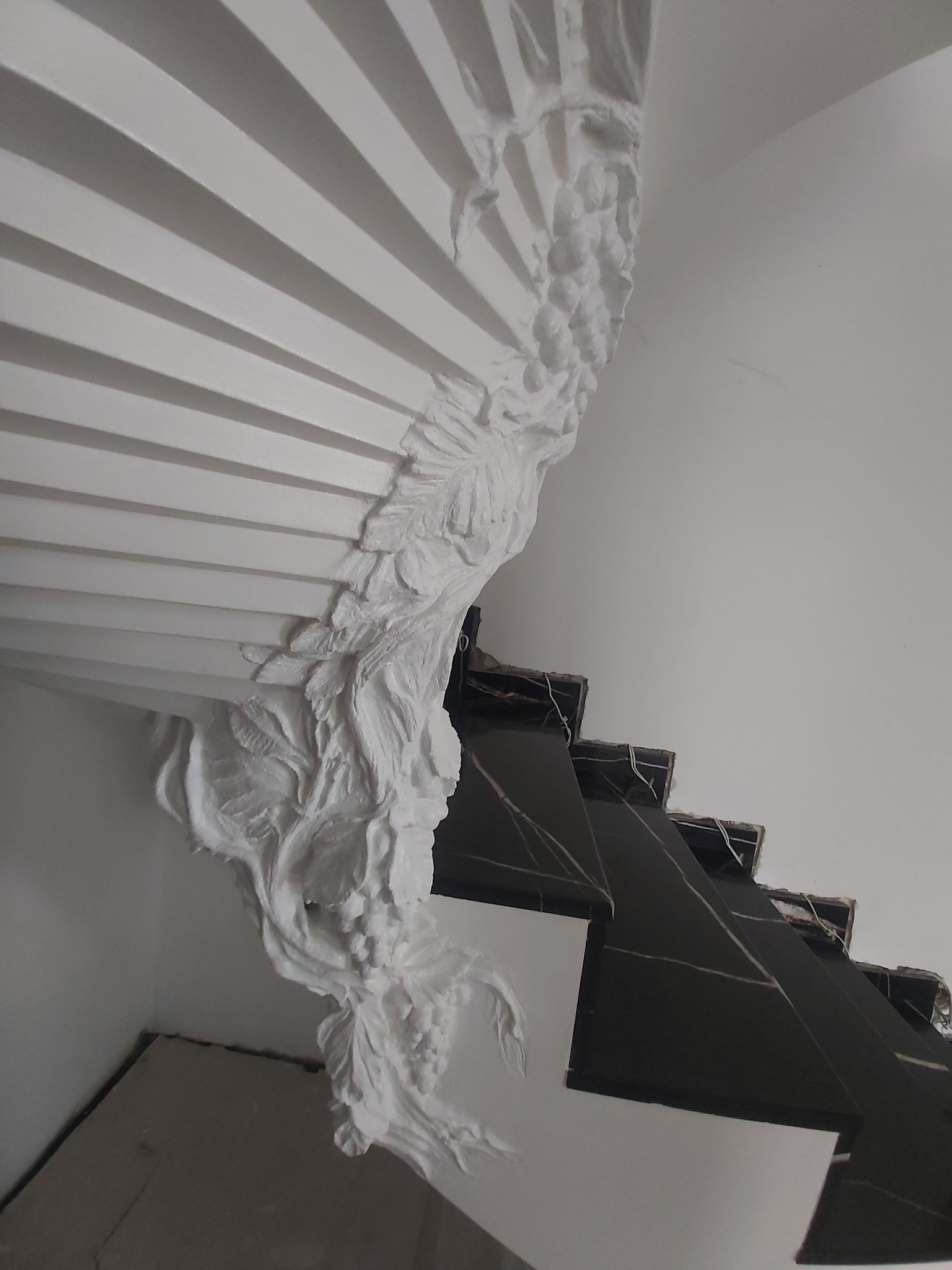 Dekoracyjny element sztukaterii z motywami roślinnymi, zdobiący schody wyłożone czarnym marmurem w trakcie montażu.