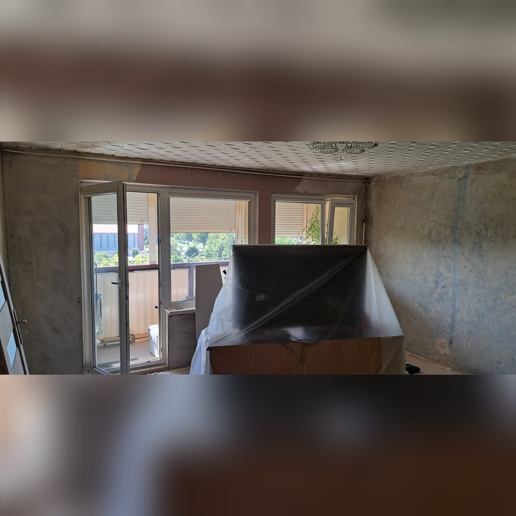 Pokój w trakcie remontu: ściany przygotowane do malowania, meble zabezpieczone folią, widoczne okno balkonowe z roletami.