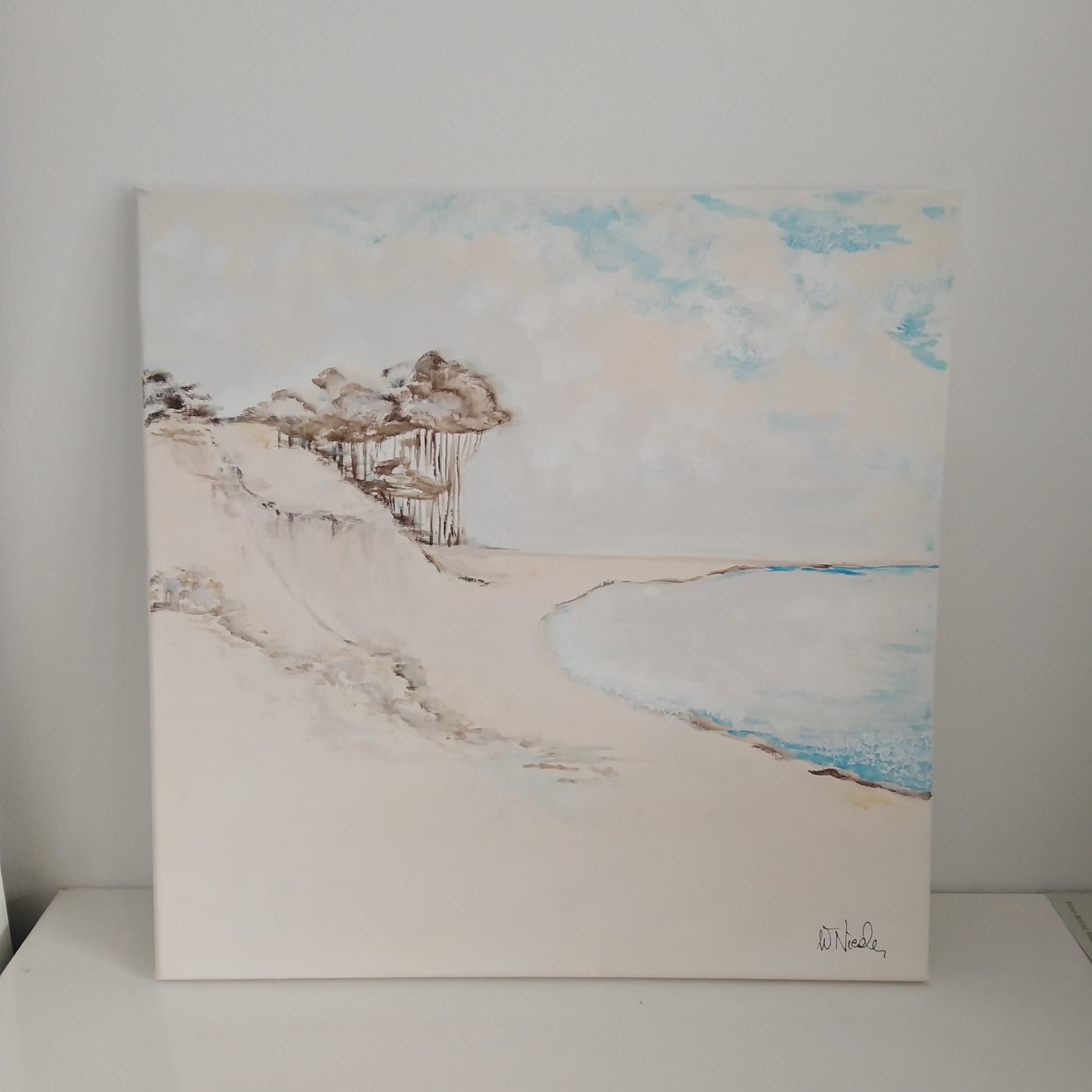 Obraz olejny przedstawiający piaszczystą plażę z klifem i drzewami, utrzymany w stonowanej kolorystyce bieli, beżu i błękitu, z widoczną sygnaturą autora w prawym dolnym rogu.