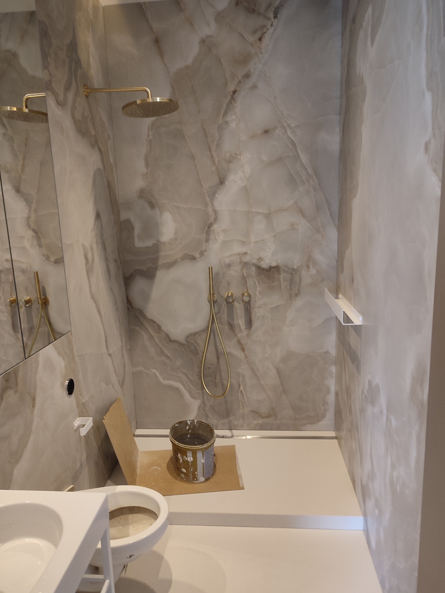 Łazienka w trakcie wykańczania z marmurowymi płytami, złotą armaturą i widocznym wiadrem z zaprawą.