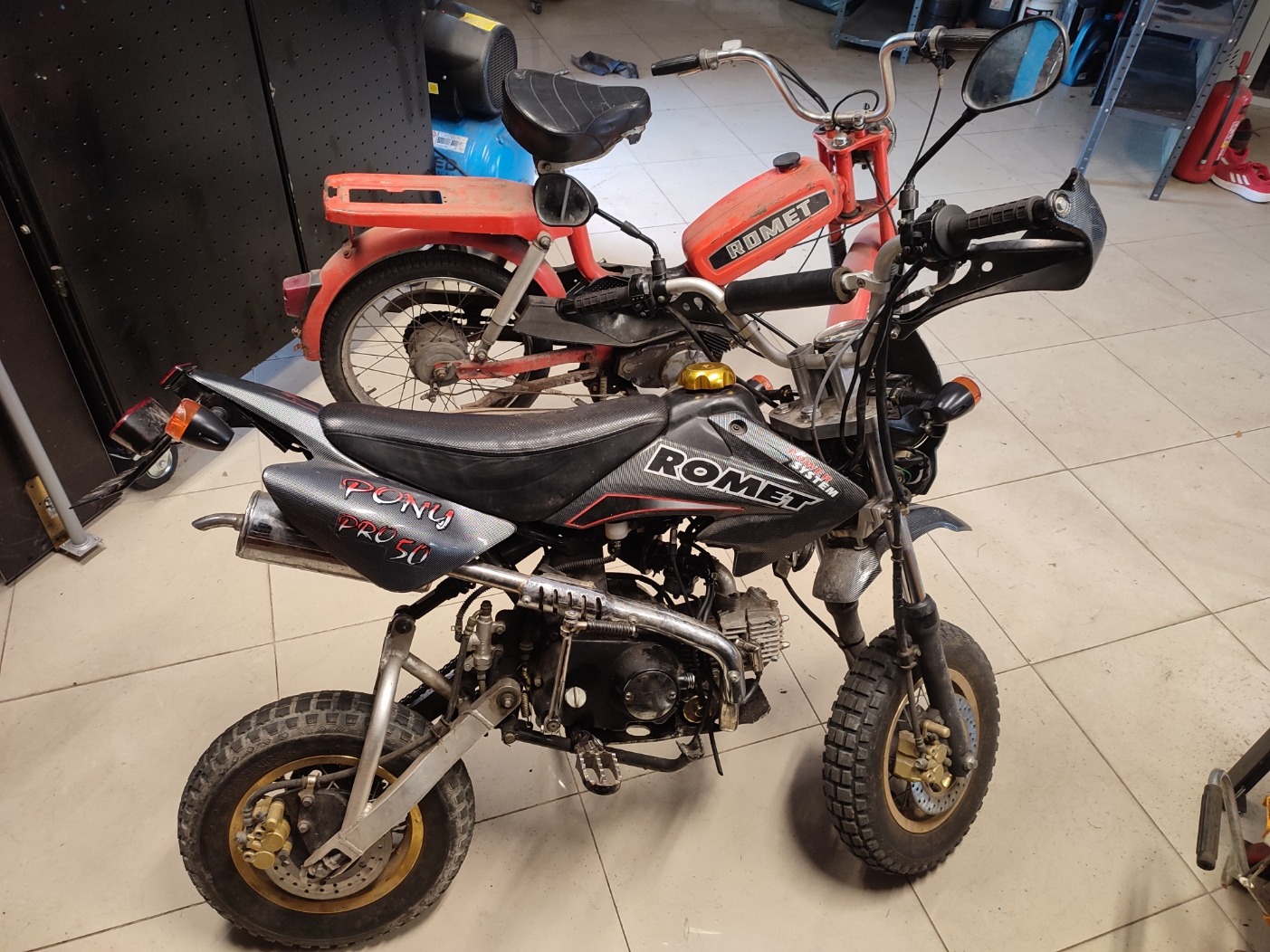 Dwa motocykle Romet, jeden czerwony starszy model, drugi czarny Pony Pro 50, stojące w warsztacie na kafelkach.