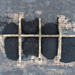 IMEX-PIECHOTA I Sp. z o.o. Sp. k. - Widok z góry na cztery pryzmy czarnego opału o różnej grubości ziarna, oddzielone betonowymi krawężnikami na placu wyłożonym kostką brukową.