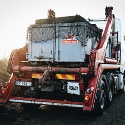 IMEX-PIECHOTA I Sp. z o.o. Sp. k. - Ciężarówka z hakiem i kontenerem na odpady, widok z tyłu, tablica rejestracyjna OP 0331T, naklejka z adresem strony internetowej na kontenerze, siatka zabezpieczająca ładunek.
