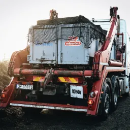 Ciężar&oacute;wka z hakiem i kontenerem na odpady, widok z tyłu, tablica rejestracyjna OP 0331T, naklejka z adresem strony internetowej na kontenerze, siatka zabezpieczająca ładunek.
