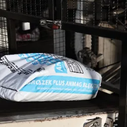 Worek z napisem 'PROSZEK PLUS ANMAG BŁĘKITN' na taśmie produkcyjnej, widoczne elementy maszyny pakującej.
