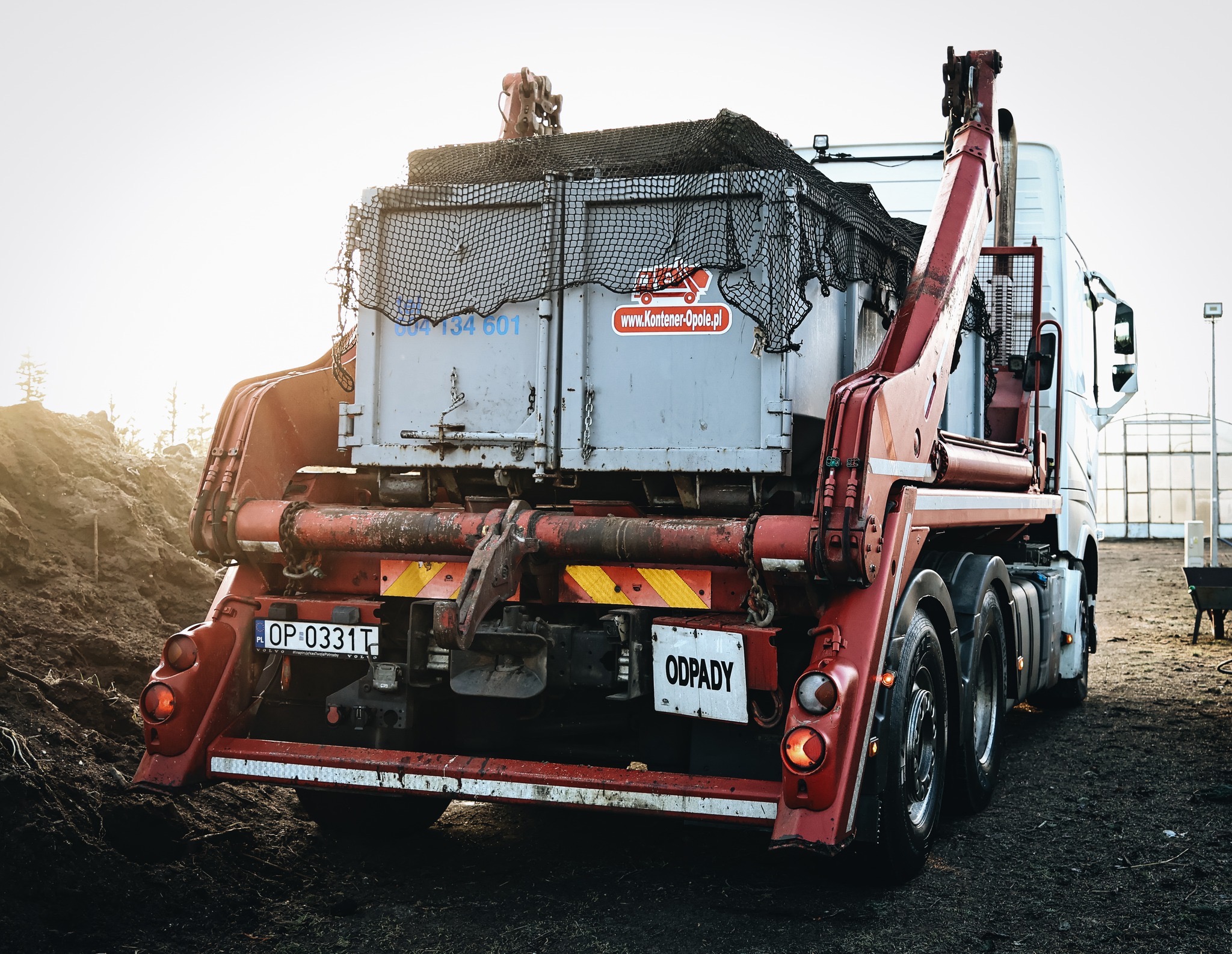 Ciężarówka z hakiem i kontenerem na odpady, widok z tyłu, tablica rejestracyjna OP 0331T, naklejka z adresem strony internetowej na kontenerze, siatka zabezpieczająca ładunek.