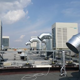 Better Climate Sp. z o.o. - Instalacja klimatyzacji na dachu budynku komercyjnego z widocznymi jednostkami zewnętrznymi i kanałami wentylacyjnymi, zabezpieczona metalową konstrukcją, widok w słoneczny dzień.
