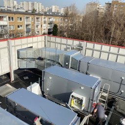 Better Climate Sp. z o.o. - Instalacja przemysłowej wentylacji na dachu budynku, widoczne kanały wentylacyjne, urządzenia i pracownik serwisu przy otwartej skrzynce sterowniczej, w tle zabudowa miejska.