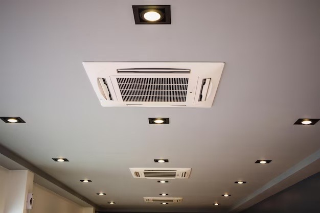 Sufit z zamontowanymi kasetonowymi klimatyzatorami i punktowym oświetleniem LED w czarnych oprawach.