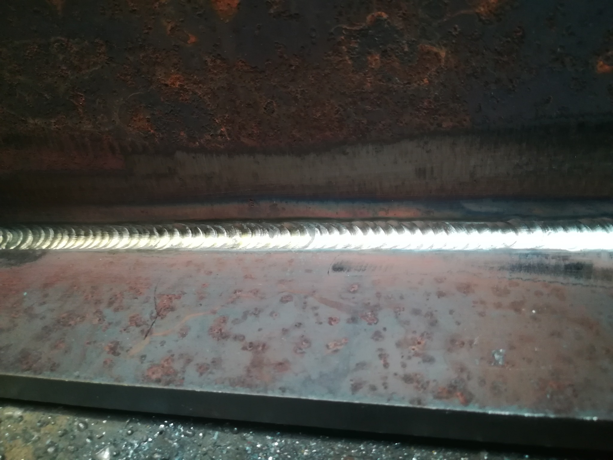 Świeżo wykonana spoina na zardzewiałej, grubej blasze stalowej, widoczne drobne odpryski po spawaniu.