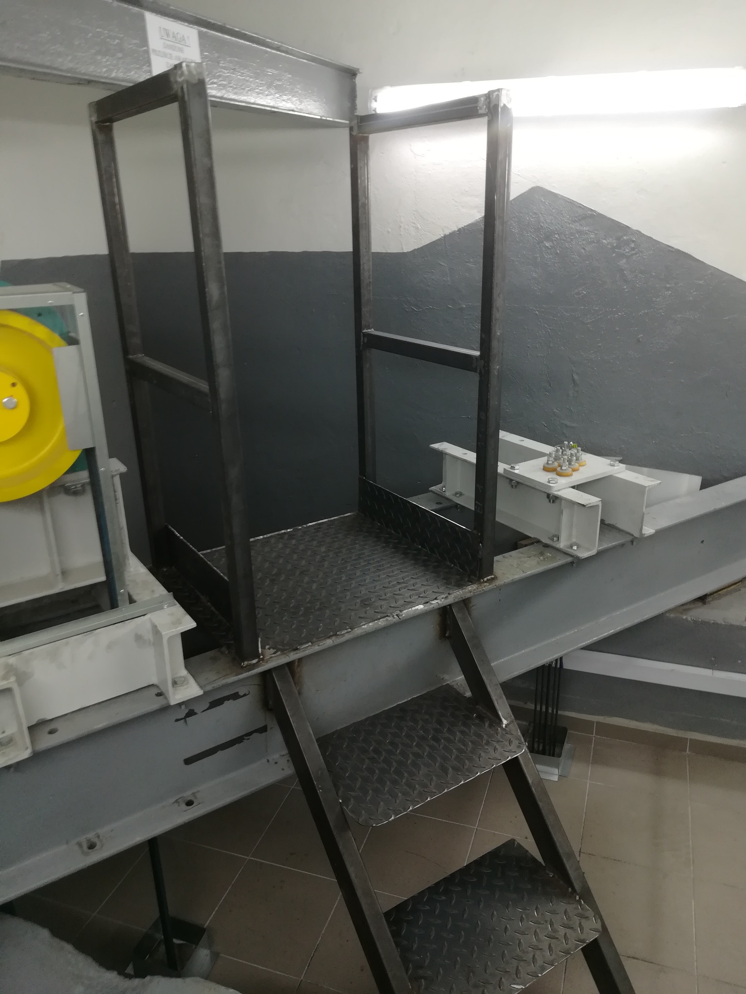 Metalowa konstrukcja schodów z platformą, spawana z profili stalowych, z widocznymi śladami spawania, zamontowana w przestrzeni przemysłowej.