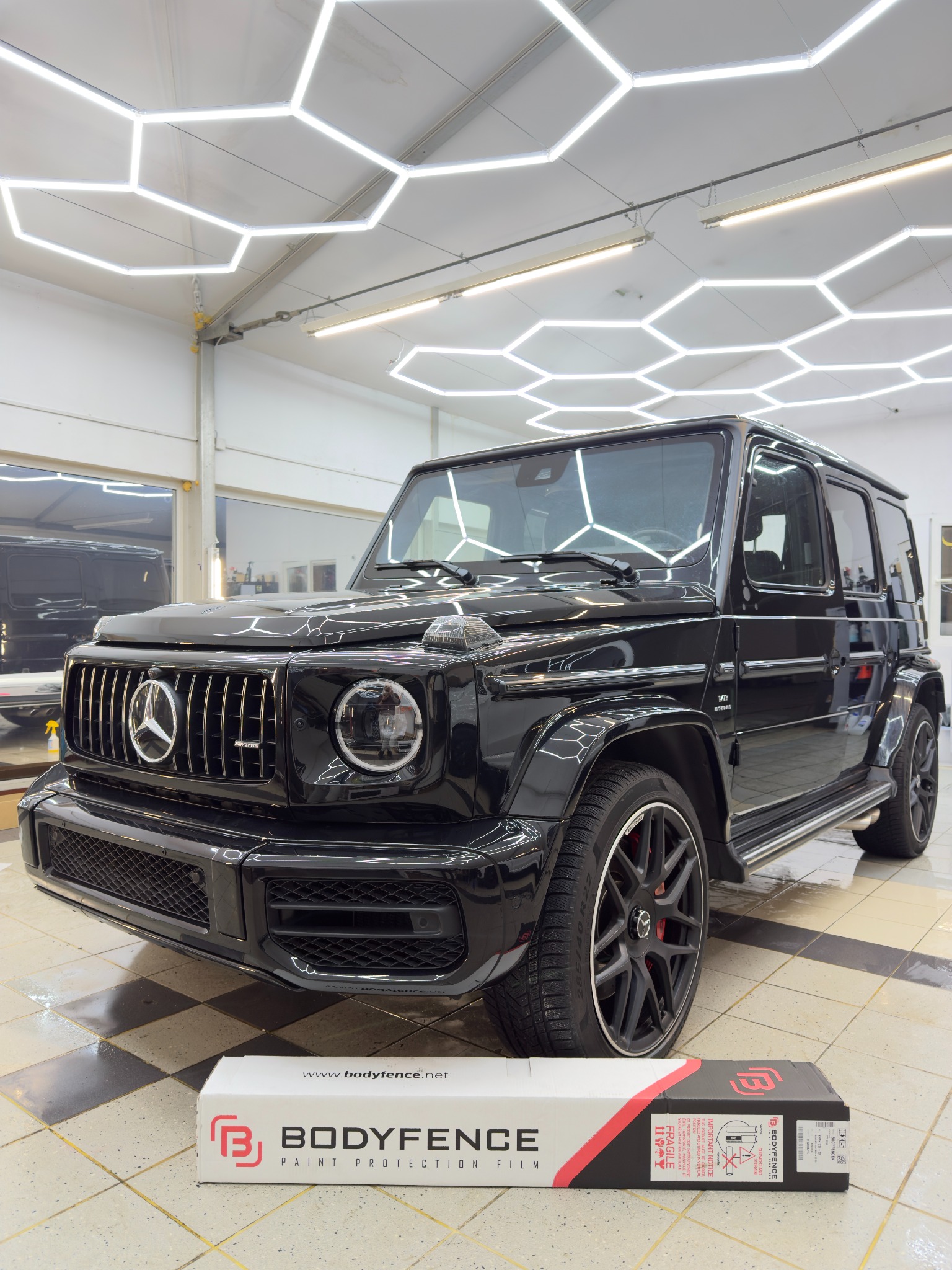 Czarny Mercedes-Benz G-klasy po aplikacji folii ochronnej PPF Bodyfence, widoczny karton z folią. Jasne oświetlenie warsztatowe.