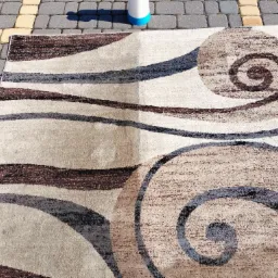 Dywan z abstrakcyjnym wzorem, częściowo wyczyszczony, leżący na kostce brukowej.