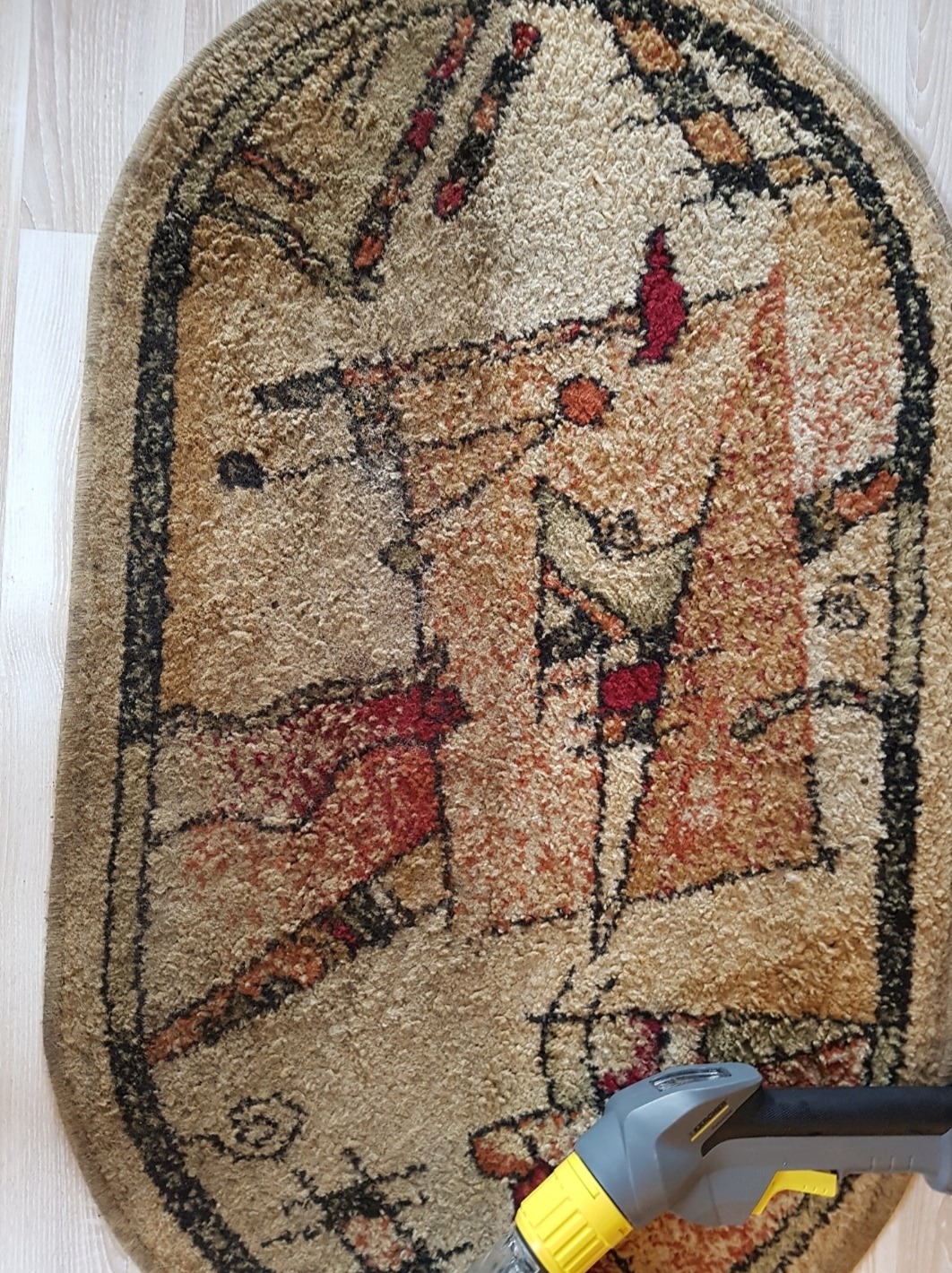 Owalny dywan z geometrycznym wzorem czyszczony odkurzaczem piorącym z żółtą końcówką na podłodze z jasnych paneli.