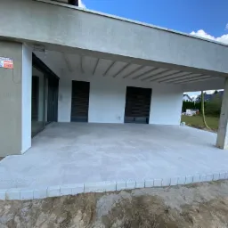 Nowoczesny taras z jasnoszarej kostki brukowej, obrzeża z kostki granitowej, widok na dom z betonowym zadaszeniem i niezabudowanym terenem.