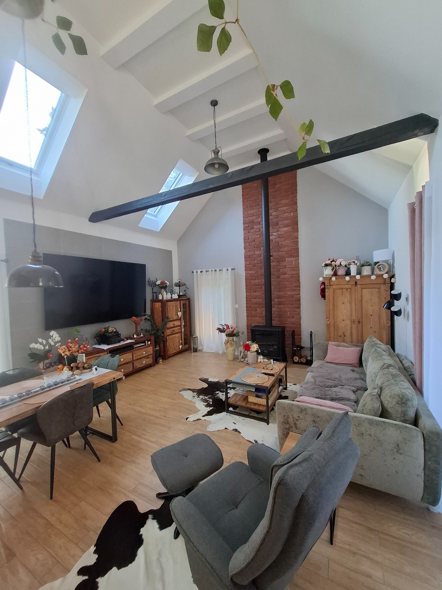 Salon z kominkiem i klimatyzacją: nowoczesne wnętrze z drewnianymi akcentami, skórzanym dywanem i dużym telewizorem. Widoczne okna dachowe i elementy dekoracyjne.