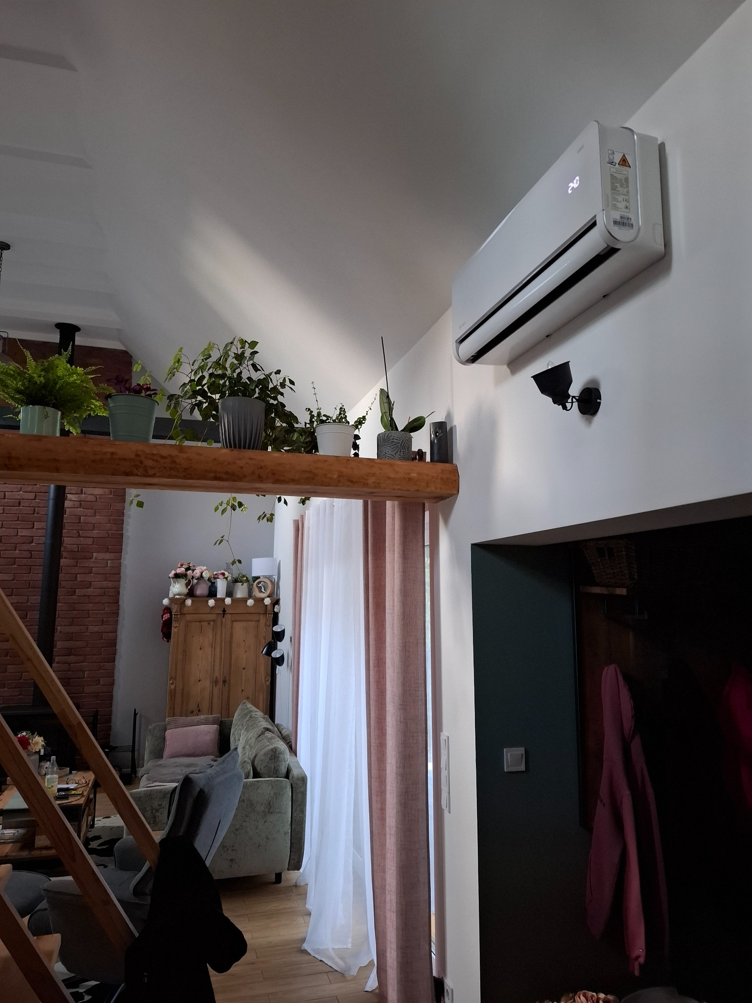 Biała klimatyzacja ścienna w jasnym wnętrzu domu z drewnianymi elementami i roślinami. Widok z dołu, nowoczesny design.