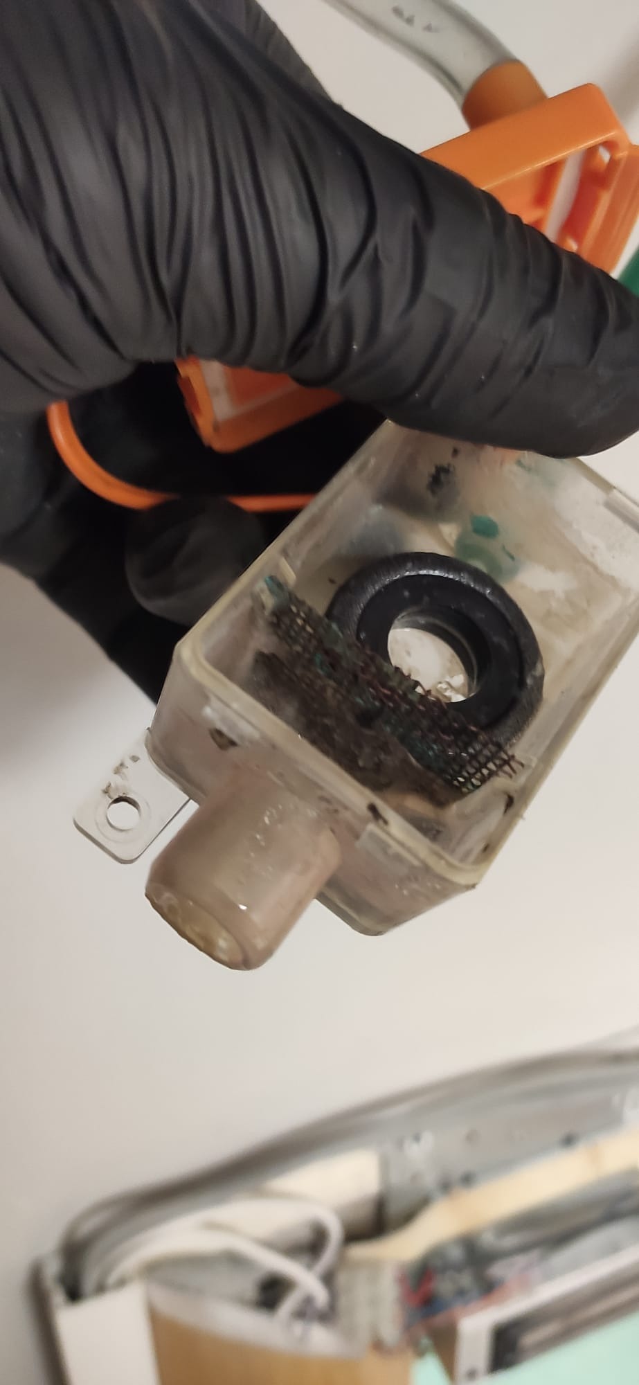 Filtr zanieczyszczeń z systemu wentylacyjnego w przezroczystym pojemniku, trzymany w dłoni w czarnej rękawicy ochronnej.