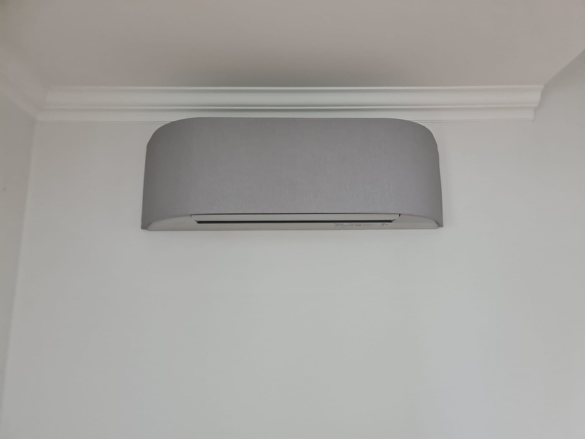 Szara jednostka wewnętrzna klimatyzacji zamontowana na białej ścianie pod ozdobnym gzymsem sufitowym.