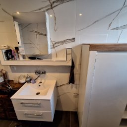 thermal komfort - Nowoczesna łazienka z białą umywalką, szafką z drewnianym blatem i lustrem. Ściany wyłożone białymi płytkami z marmurkowym wzorem. Elementy dekoracyjne dodają przytulności.