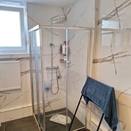 thermal komfort - Nowoczesna kabina prysznicowa z deszczownicą, wykończona marmurowymi płytkami z brązowymi żyłami. Na zewnątrz wieszak na ręczniki.