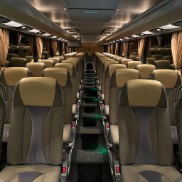 X-Bus Sp. z o. o. Sp. K. - Wnętrze autobusu w Sucha Beskidzka z rzędami foteli w odcieniach brązu i beżu, oświetlonych delikatnym światłem, z widocznymi zasłonami w oknach.