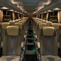 Wnętrze autobusu w Sucha Beskidzka z rzędami foteli w odcieniach brązu i beżu, oświetlonych delikatnym światłem, z widocznymi zasłonami w oknach.