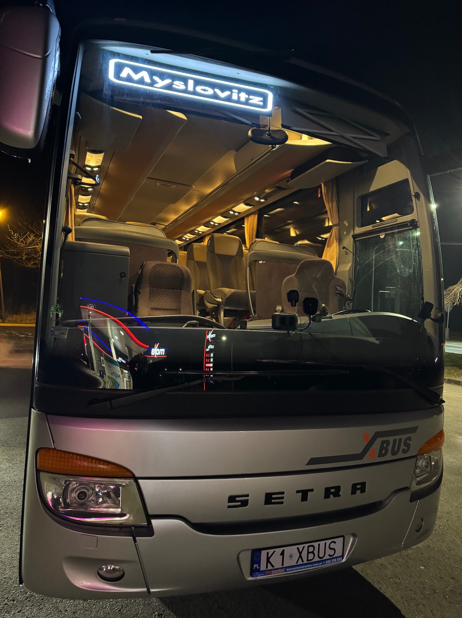 Przód srebrnego autokaru Setra z podświetlonym napisem 'Myslovitz' nad szybą, widok na wnętrze z fotelami pasażerskimi.