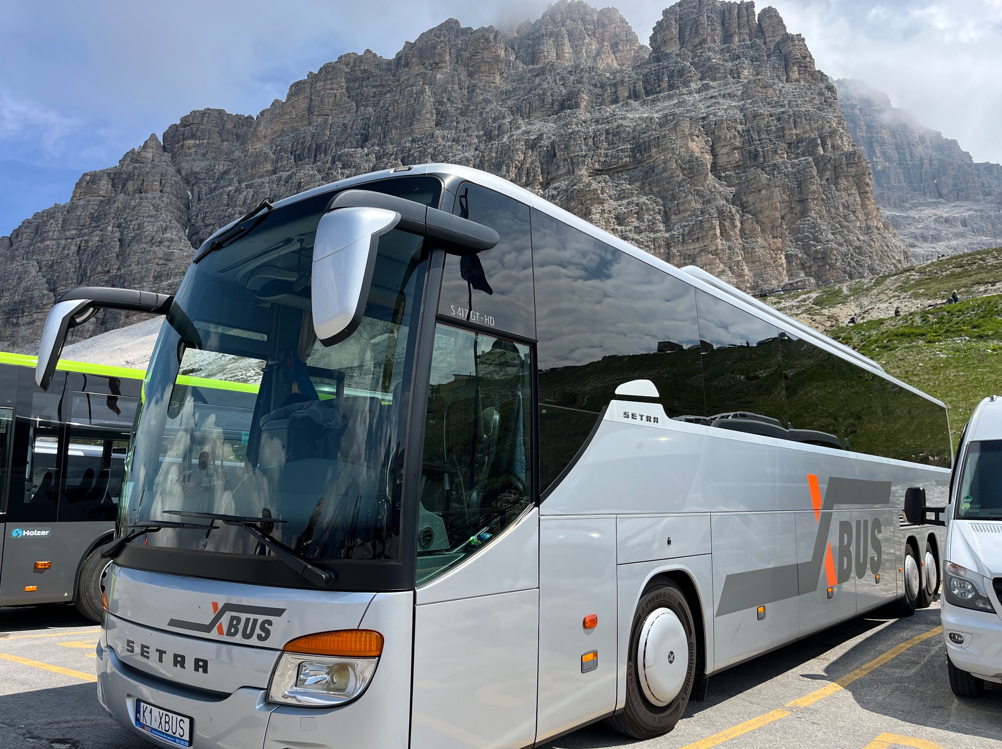 Srebrny autokar Setra XBUS z pomarańczowym logo na tle skalistych gór w słoneczny dzień.