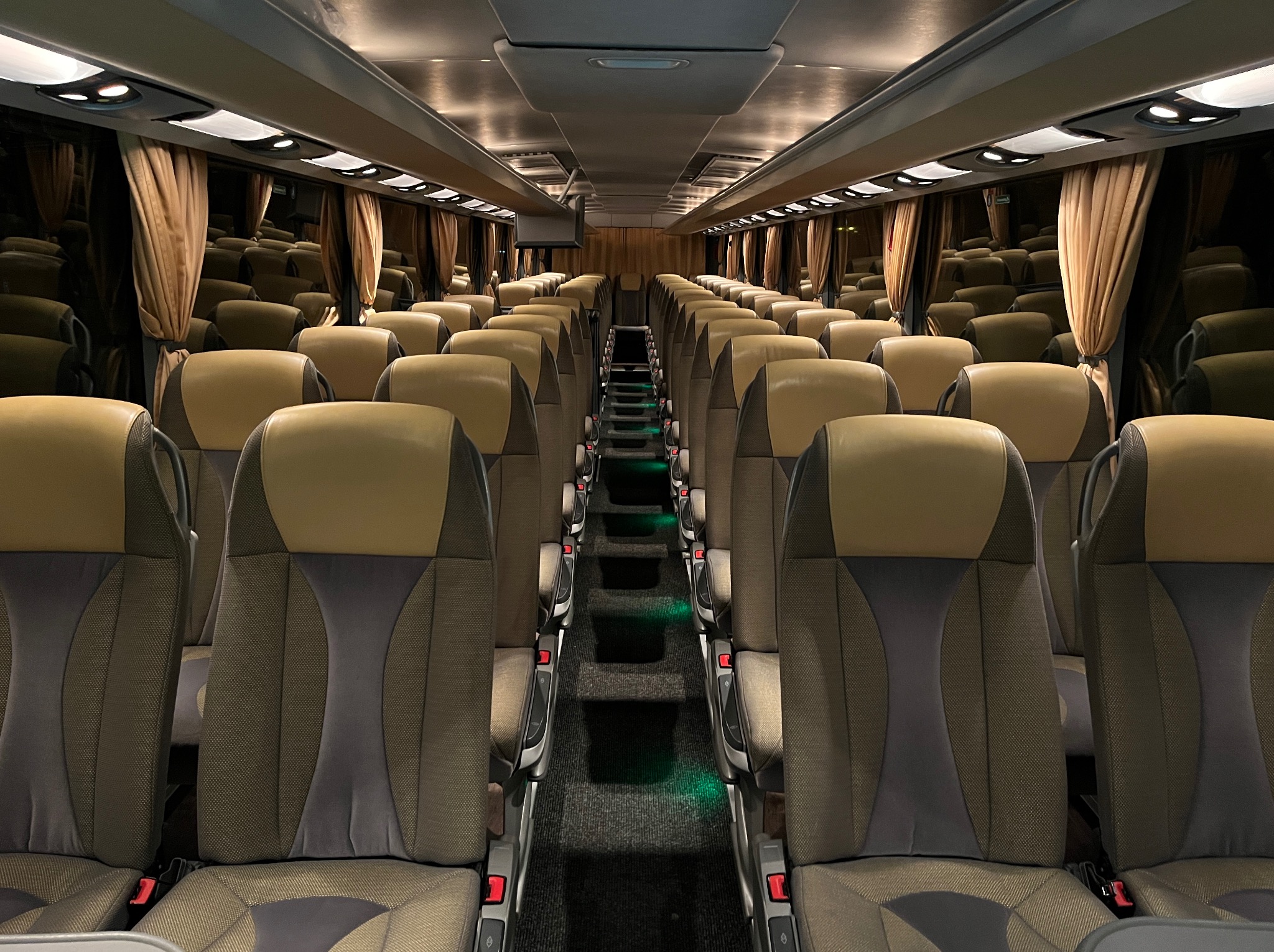 Wnętrze autobusu w Sucha Beskidzka z rzędami foteli w odcieniach brązu i beżu, oświetlonych delikatnym światłem, z widocznymi zasłonami w oknach.