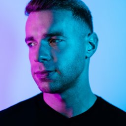 dabrowskistudio.pl Arkadiusz Dąbrowski - Portret mężczyzny z krótkimi włosami, oświetlonego niebiesko-różowym światłem, spoglądającego w lewo, ubrany w czarny T-shirt.