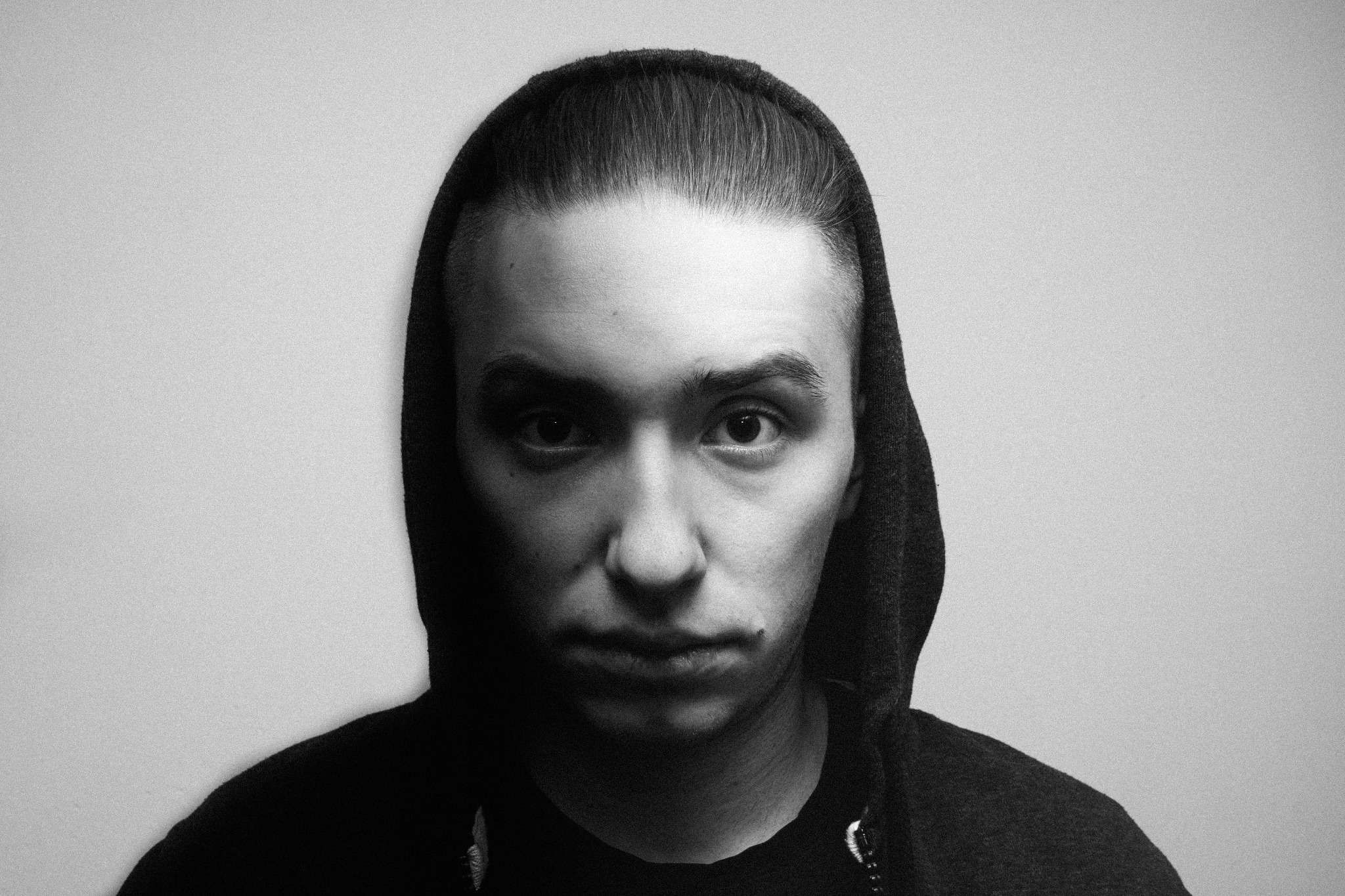 Portret młodego mężczyzny w kapturze, czarno-biały, oświetlenie studyjne, z zaczesanymi do tyłu włosami i poważnym wyrazem twarzy.