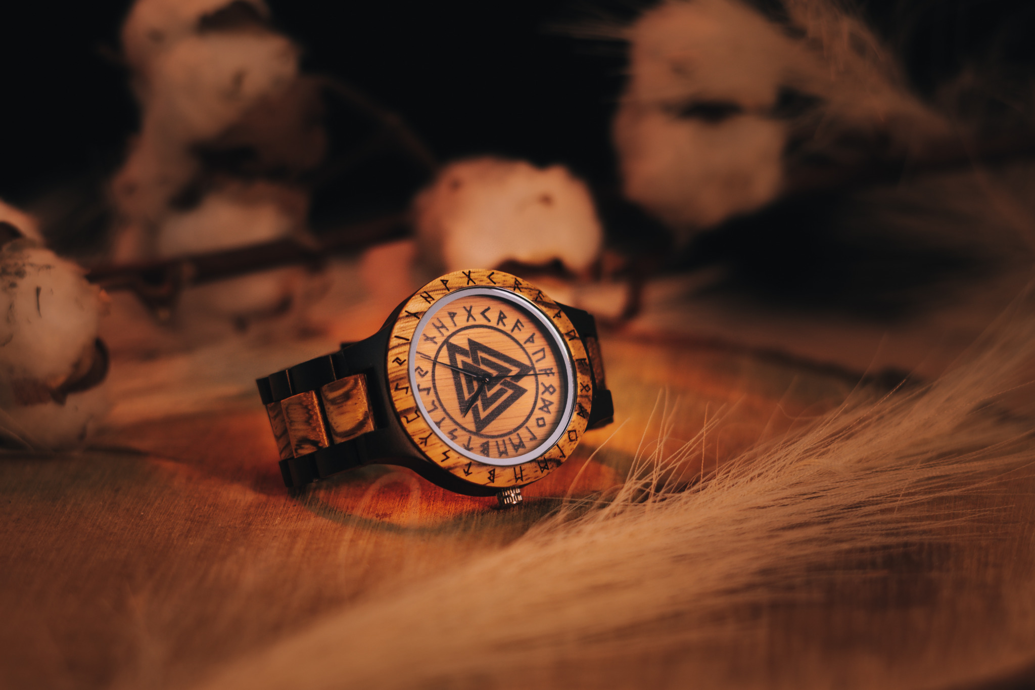 Drewniany zegarek z runami i symbolem Walknut na tarczy, leżący na drewnianej powierzchni z dekoracyjnymi trawami i gałązkami bawełny w tle.