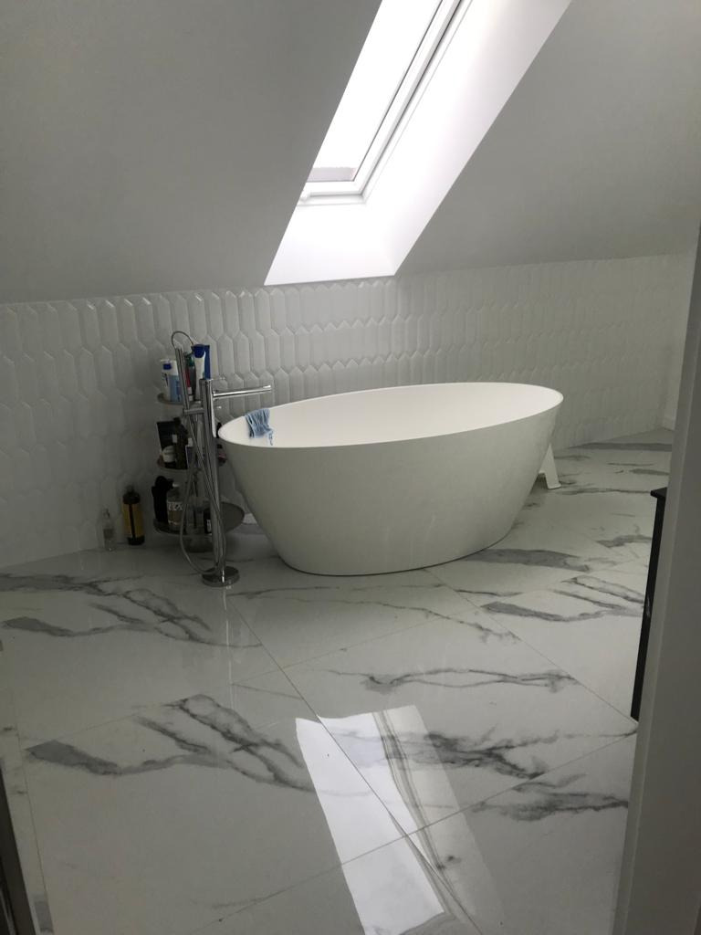 Nowoczesna łazienka na poddaszu z wolnostojącą białą wanną, biało-szarą marmurową podłogą, białą mozaiką na ścianie i oknem dachowym.