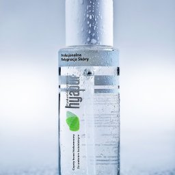 Studio Migafka - Butelka serum hialuronowego 'hyapur intense' z kroplami wody na powierzchni, umieszczona na mokrej, błyszczącej powierzchni, w tle rozmyte, jasne tło.