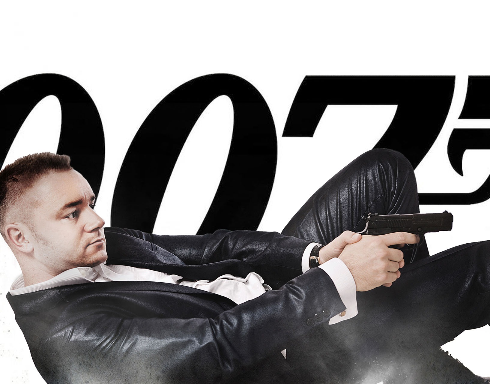 Mężczyzna w czarnym garniturze i białej koszuli, leżący na boku z pistoletem w ręku na tle logo 007.