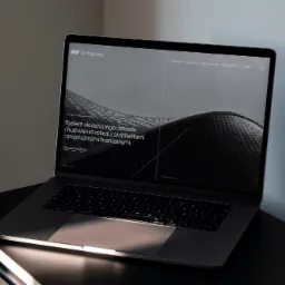 Laptop wyświetlający stronę internetową Archispace z tekstem o budowaniu relacji z architektami, umieszczony na czarnym stoliku.