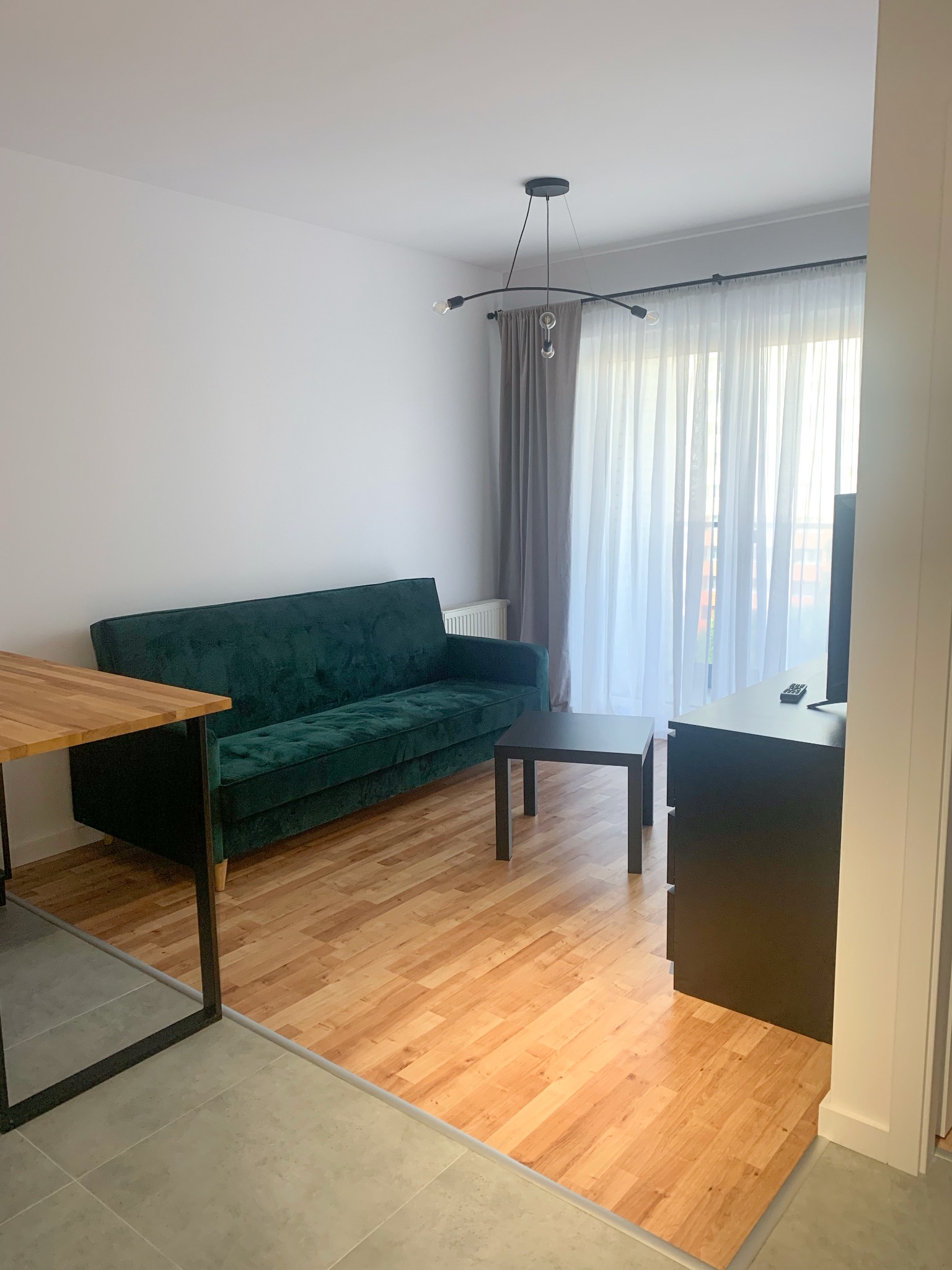 Nowoczesny salon z parkietem w jodełkę, zieloną sofą, stolikiem kawowym i lampą sufitową z żarówkami Edison