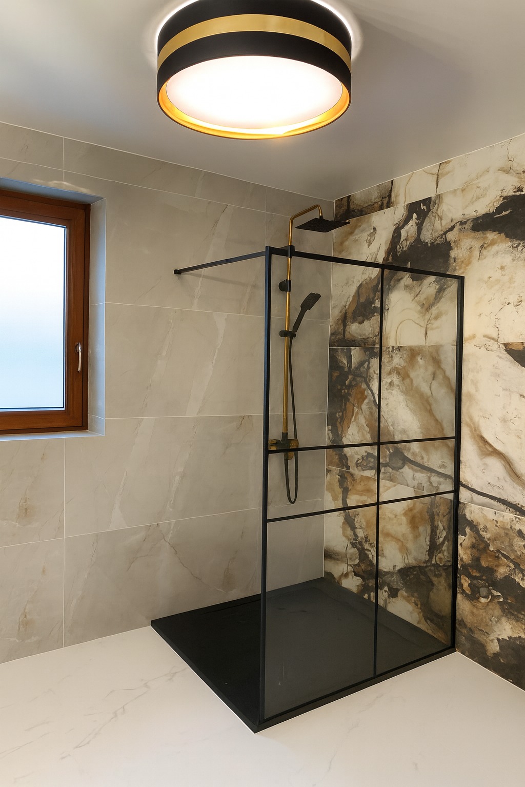 Nowoczesna kabina prysznicowa z czarną ramą i złotą armaturą na tle marmurowych płytek w beżach i brązach. Okno z drewnianą ramą.