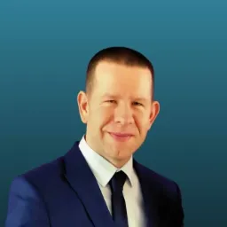 Portret uśmiechniętego mężczyzny w ciemnoniebieskim garniturze i czarnym krawacie na jednolitym niebieskim tle.