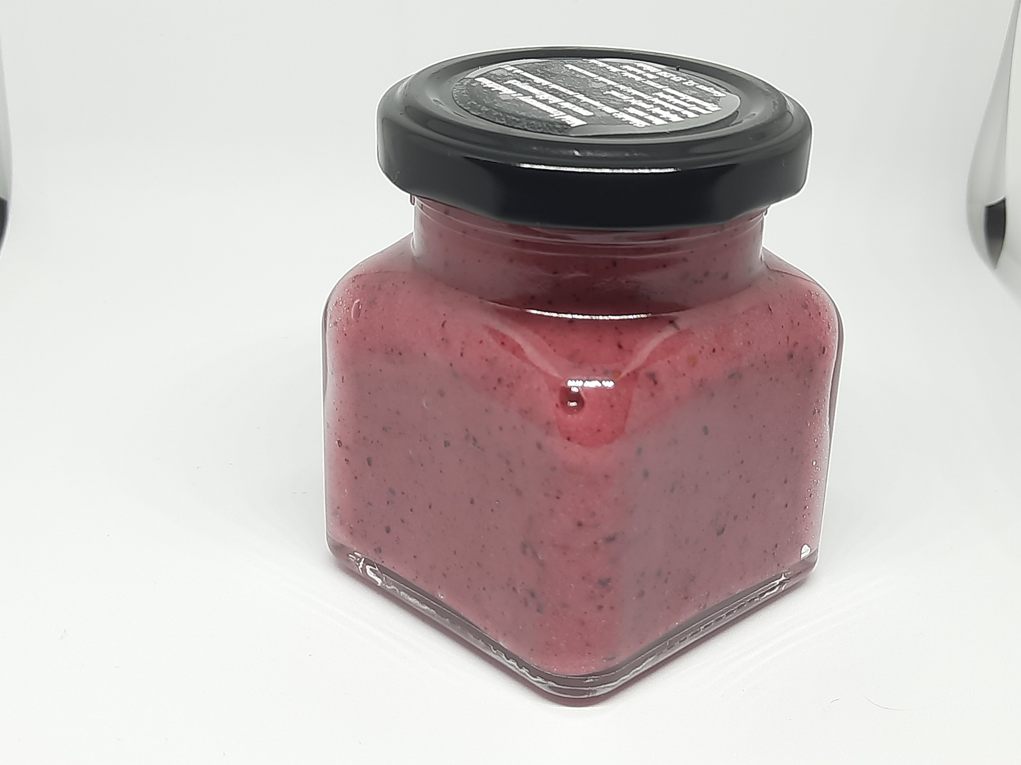 Kwadratowy słoik z ciemnoróżową zawartością o widocznej strukturze, zamknięty czarną zakrętką z naklejką, na białym tle.