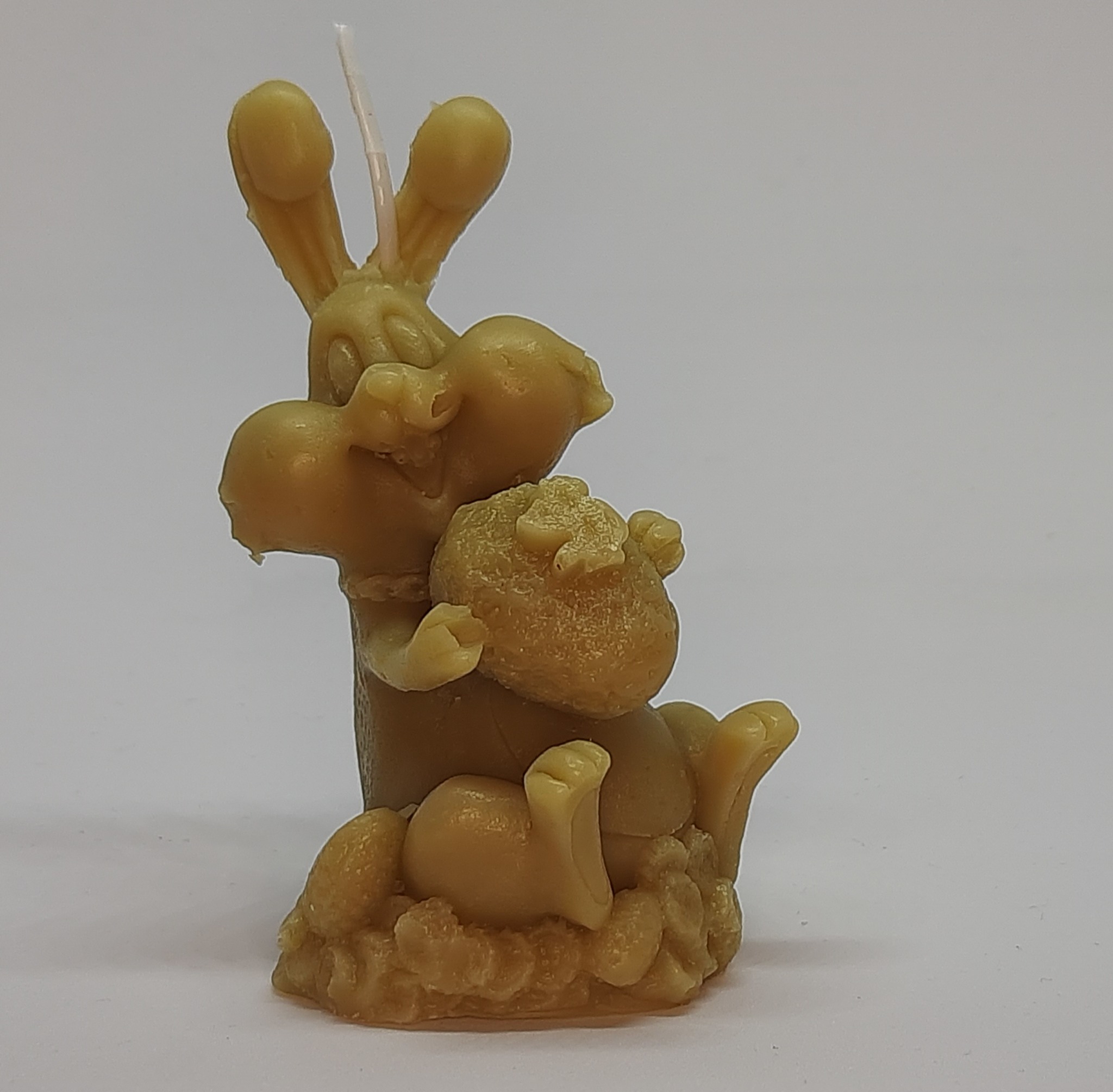 Ręcznie wykonana świeca z wosku pszczelego w kształcie królika trzymającego worek, na białym tle.