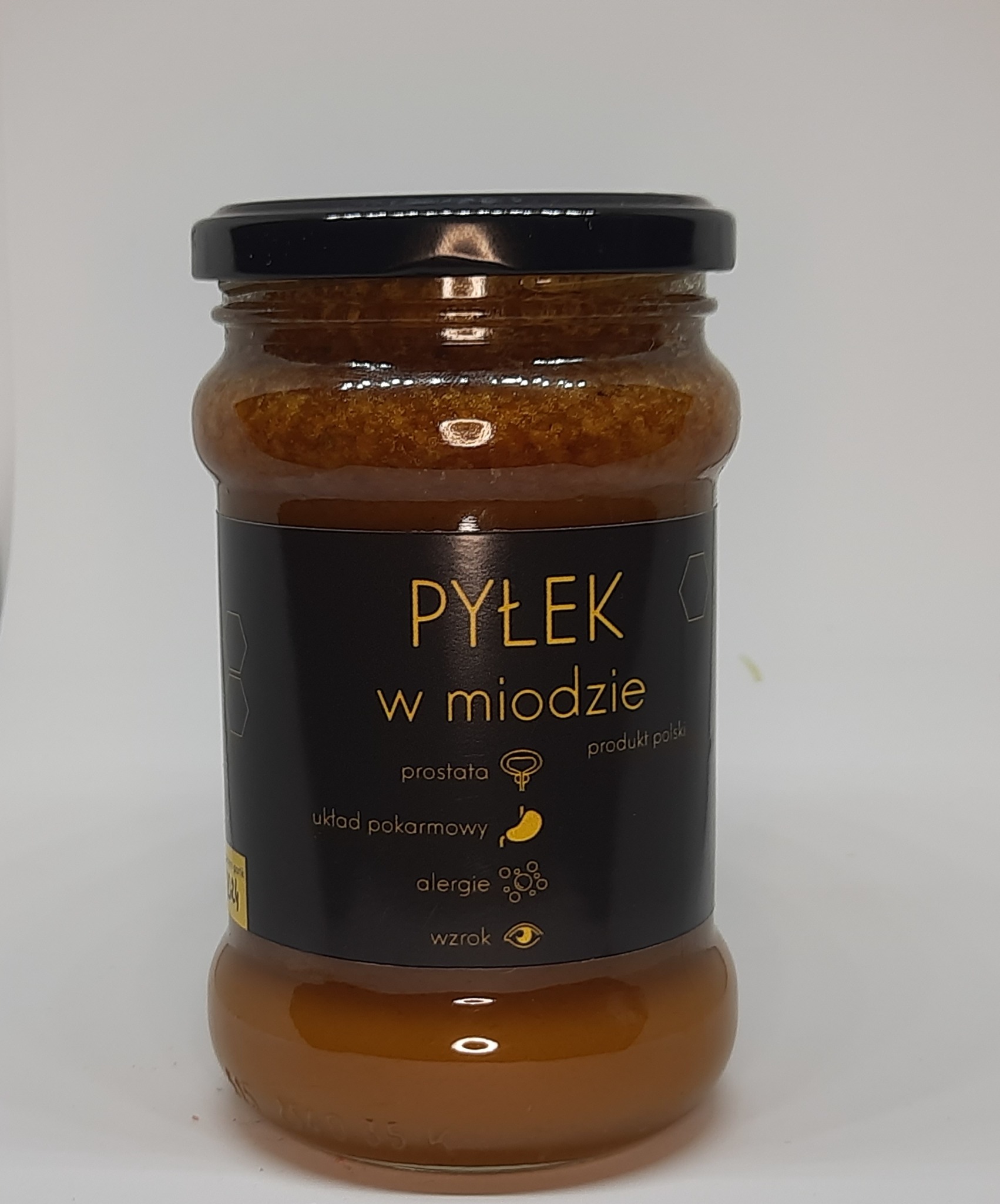 Słoik z pyłkiem w miodzie, etykieta z informacjami o produkcie i wskazaniami zdrowotnymi, czarna zakrętka.