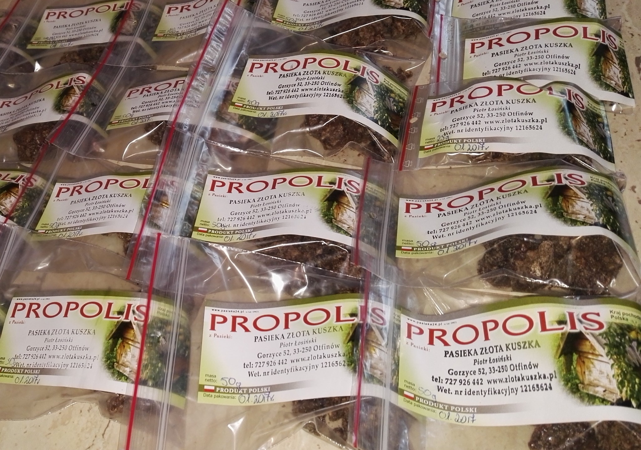 Wiele małych, przezroczystych woreczków z propolisem, każdy oznaczony etykietą 'Pasieka Złota Kuszka', ułożonych rzędami.