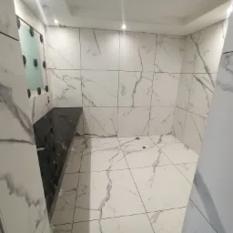 Wykończona łazienka we Władysławowie z płytkami imitującymi marmur na ścianach i podłodze, czarny blat umywalkowy i fragment lustra z przyssawkami.