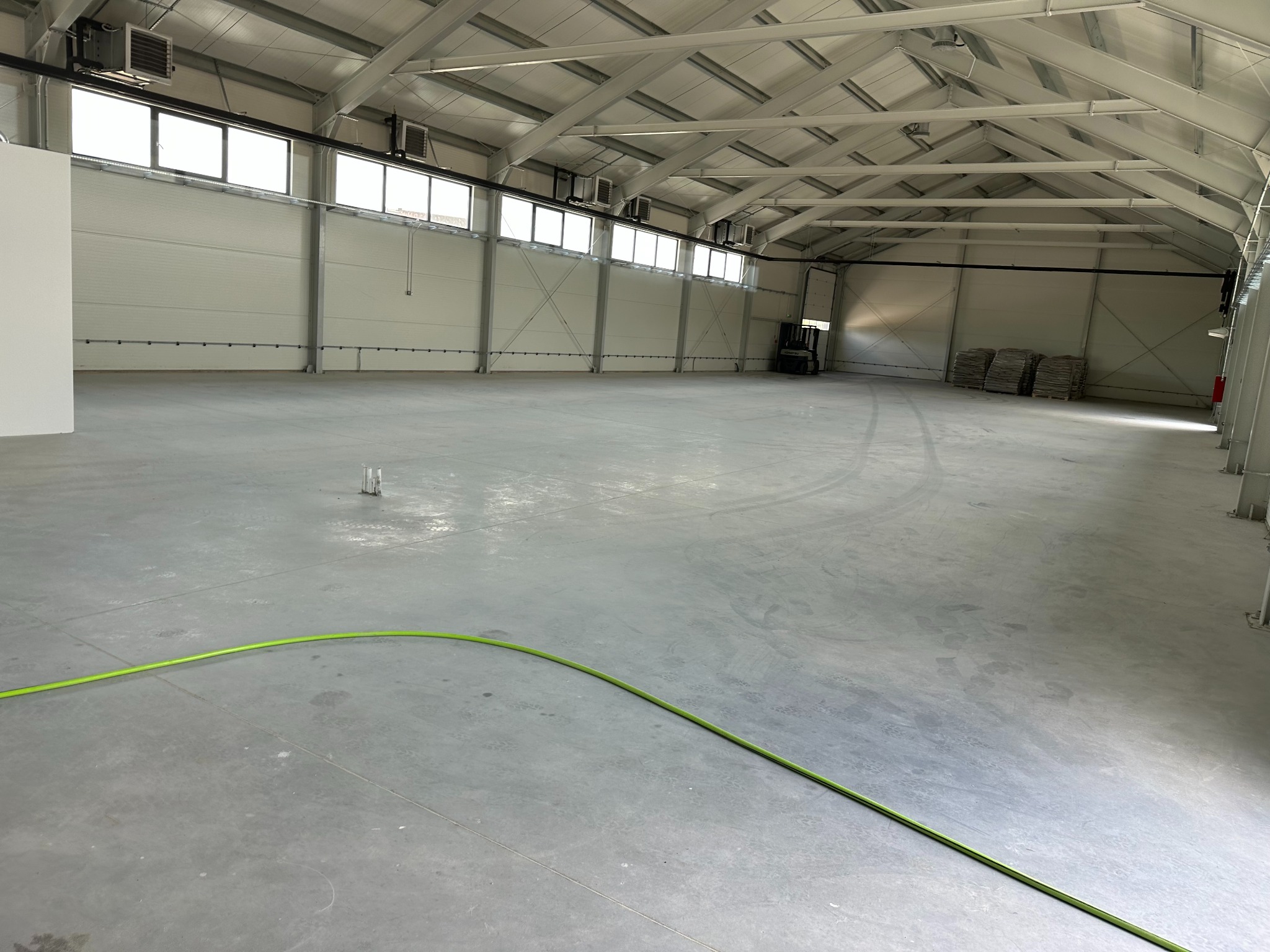 Wnętrze hali magazynowej w Olsztynie z betonową posadzką, widoczne ślady opon, w tle wózek widłowy i worki, oświetlenie górne.