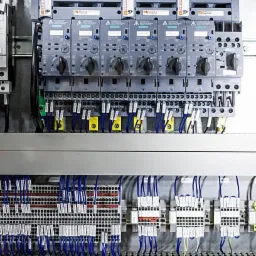 Szczegółowe ujęcie rozdzielnicy elektrycznej z widocznymi zabezpieczeniami, okablowaniem i elementami sterującymi, charakteryzujące się precyzyjnym ułożeniem przewodów i komponentów.