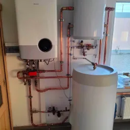 Nowoczesny piec grzewczy Hisense z dwoma zasobnikami ciepłej wody, połączony miedzianymi rurami, zainstalowany w pomieszczeniu z grzejnikiem i oknem.